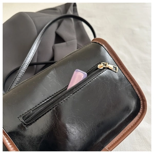 Détail d'un sac à bandoulière noir avec bordure marron et poche zippée fonctionnelle