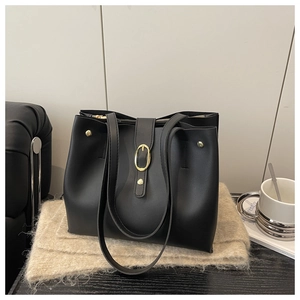 Close-up of black soft leather tote bag with gold oval buckle on a cozy table setting
