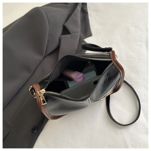 Interior view of black crossbody bag with brown piping showing storage for phone and lipstick