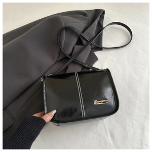 Détail du sac en cuir verni noir avec coutures blanches contrastées et logo en métal doré