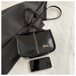 Détail du sac bandoulière en cuir verni noir avec coutures blanches et logo doré
