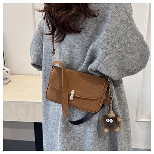 Detail of vintage brown crossbody bag featuring a golden peanut buckle and fuzzy charm