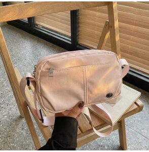 Pink nylon crossbody bag with adjustable strap shown on a wooden chair in soft daylight