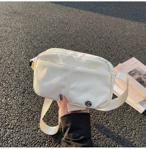 Detail of off-white waterproof nylon chest bag with dual front pockets on asphalt surface