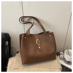 Close-up of brown leather tote bag featuring gold buckle details on a knit surface