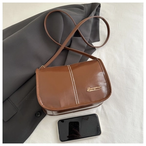 Détail du sac bandoulière marron foncé avec surpiqûres blanches et logo en métal doré