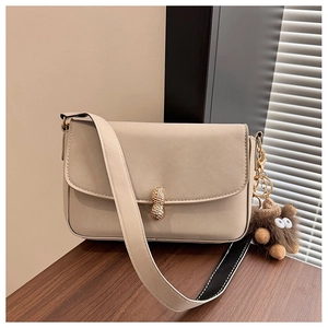 Detail of beige leather shoulder bag featuring a unique gold peanut buckle and plush charm