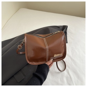 Détail du sac bandoulière en similicuir marron avec coutures blanches et logo doré