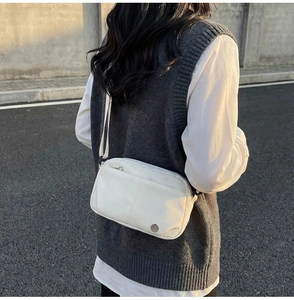 Détail d'un sac bandoulière blanc cassé avec coutures symétriques et logo métallique
