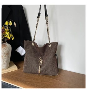Sac bandoulière marron scintillant avec finitions dorées et pompon dans un décor studio