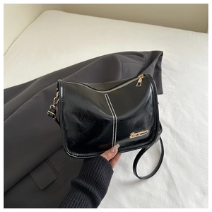 Détail du sac bandoulière noir minimaliste avec couture blanche et logo en métal doré