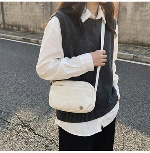 Close-up of beige crossbody bag with adjustable strap and metal logo detail