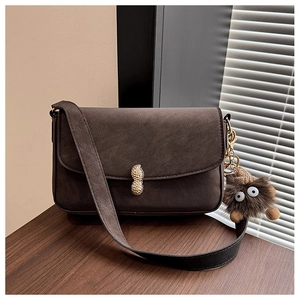 Detail of dark brown baguette bag featuring a peanut-shaped gold lock and fuzzy monster charm