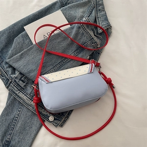 Chic blue crossbody bag with white polka dot flap and vibrant red shoulder strap