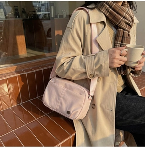 Close-up of light pink nylon crossbody bag with wide strap and circular logo detail