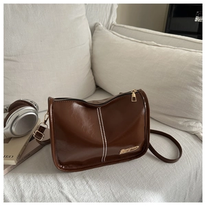Détail du sac bandoulière en cuir brillant marron foncé avec surpiqûres blanches