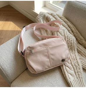 Close-up of a light pink nylon crossbody bag with a front zipper pocket on a soft sofa