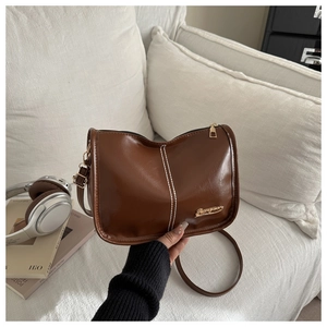 Détail du sac bandoulière en cuir PU brillant marron avec coutures blanches et métal doré