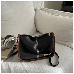 Détail du sac bandoulière en cuir verni noir avec garniture brune et boucles dorées
