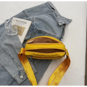 Close-up of bright yellow nylon crossbody bag with three zippers on denim background