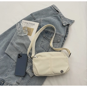 Detail of off-white crossbody bag with adjustable strap on denim jacket and art book