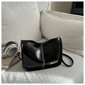Détail du sac à bandoulière noir brillant avec surpiqûres blanches et finitions dorées
