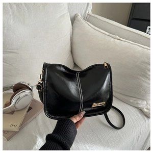 Détail du sac à bandoulière noir brillant avec coutures blanches et garniture dorée