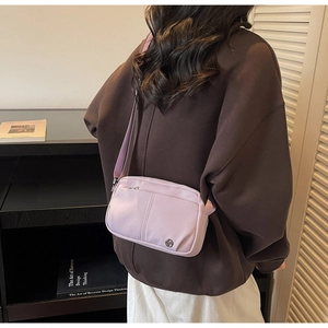 Close-up of lavender nylon crossbody bag with zipper pocket and metal logo shown on model