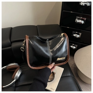 Détail du sac à bandoulière en cuir verni noir avec surpiqûres blanches et logo doré