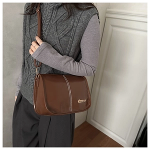 Detail view of dark brown patent leather shoulder bag with white stitching and gold logo
