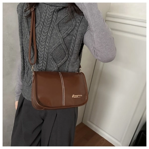 Détail du sac bandoulière marron avec surpiqûres blanches et logo doré sur le devant