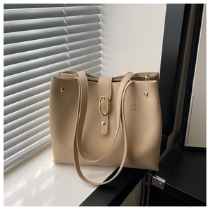 Detail of beige textured tote bag with golden oval buckle and soft window light shadows