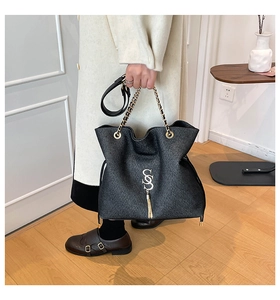 Détail du sac à bandoulière en cuir noir avec logo S en métal et franges sur manteau
