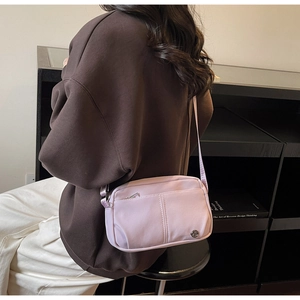 Detail of a pastel purple nylon crossbody bag with front zipper and metal logo charm