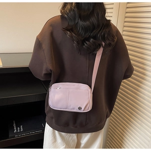 Light purple nylon crossbody bag with adjustable strap and circular metal logo detail