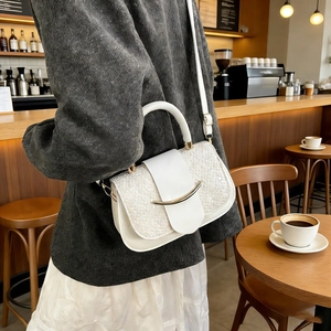 Detailed view of a white woven leather handbag featuring a curved gold metal buckle on table