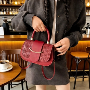 Detail einer tiefroten Handtasche mit gewebter Klappe und goldenem Metallverzierung