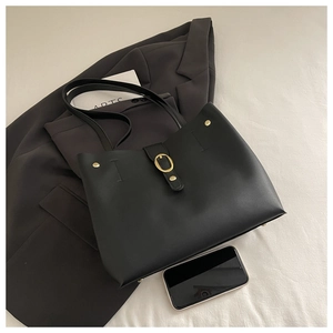 Detail view of large black leather bucket bag with gold buckle and smartphone for scale