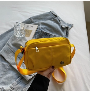 Close-up of a bright yellow nylon crossbody bag with wide shoulder strap on beige background