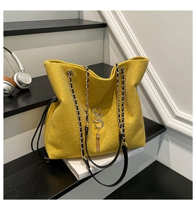 Detail of yellow glitter tote bag with chain strap, metallic S charm and fringe accent