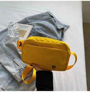 Detail of a bright yellow nylon crossbody bag with zipper and adjustable strap
