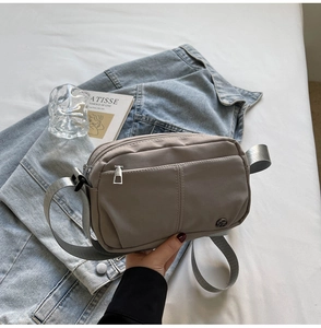 Detail of taupe water-resistant nylon crossbody bag with dual silver zippers and logo