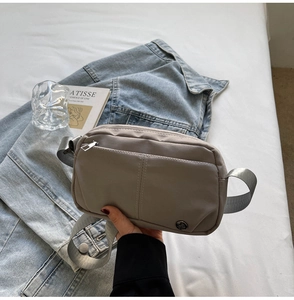 Close-up of gray nylon crossbody bag with zipper pocket and metal logo in a lifestyle setting