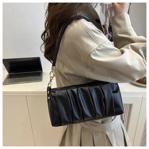 Close-up of black pleated baguette bag with woven strap and gold-tone hardware