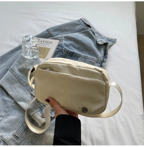 Detail of a beige minimalist crossbody bag with front zipper pocket on a lifestyle background