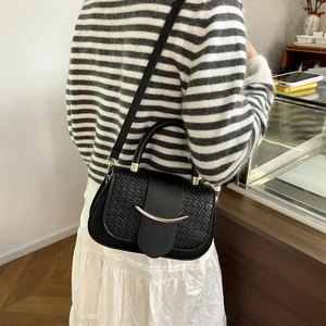 Detail of black woven texture shoulder bag with gold metal buckle on a female model