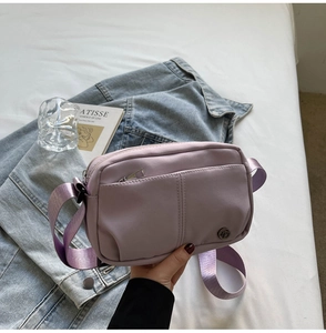 Close-up of light purple nylon crossbody bag featuring front zipper pocket and metal logo