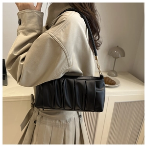 Detail of black pleated cloud bag with woven shoulder strap and golden metal ring