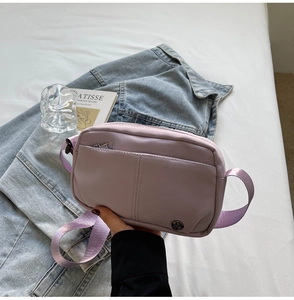 Detail of lavender square crossbody bag with metallic logo and woven shoulder strap
