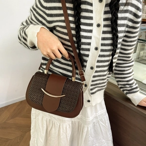 Detailed view of brown crossbody bag featuring textured woven flap and gold metal hardware